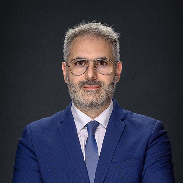 uomo con barba e capelli grigi, indossa un completo blu con cravatta e occhiali. Ha un'espressione seria e professionale, sfondo scuro. immagine realizzata per l' offerta business headshot di bruno granzotti fotografo